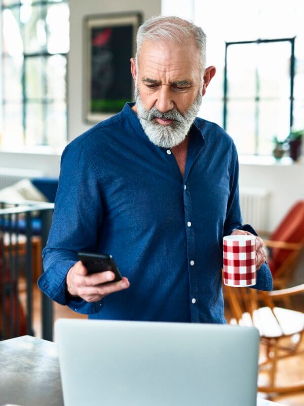 Mature man looking at his phone while holding a hot drink
