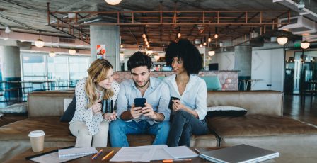 Three colleagues looking at a smartphone together during a break at the office