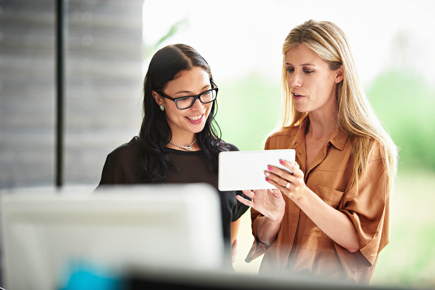 Two colleagues talking in an office while looking at employment verification information on a tablet