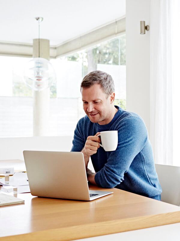 Man smiling at his laptop holding a hot drink
