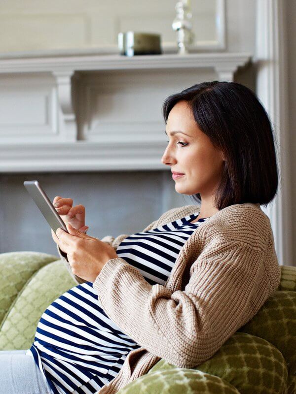 Pregnant woman looking at a tablet while laying on a sofa